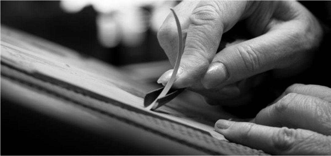 Black and white image of artist’s hands carving linoleum block.